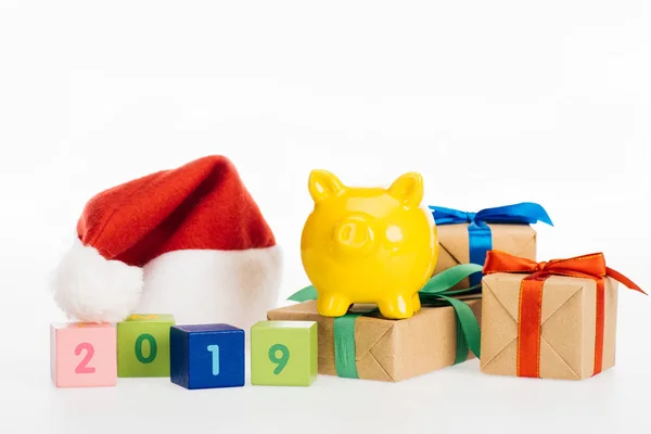 Vista close-up do símbolo 2019 em cubos, banco piggy amarelo, caixas de presente e chapéu de Papai Noel isolado em branco — Fotografia de Stock