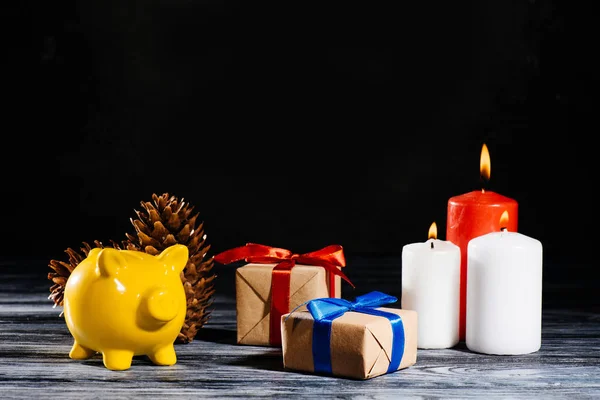 Alcancía amarilla, conos de pino, regalos de Navidad y velas encendidas - foto de stock