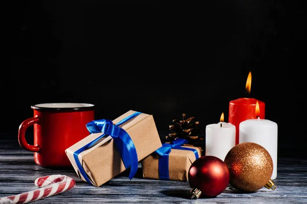 Nahaufnahme brennender Kerzen, Tannenzapfen, Weihnachtskugeln und Geschenke auf Holztisch auf schwarz — Stockfoto