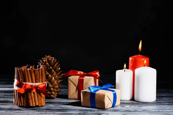 Close-up view of burning candles, pine cone and christmas gifts on wooden table on black — Stock Photo