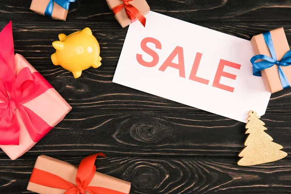 Top view of sale sign, yellow piggy bank and christmas presents on wooden surface — Stock Photo