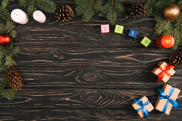Верхний вид символа 2019 года на кубиках, рождественских подарках, свечах и еловых ветках с безделушками и сосновыми шишками на деревянной поверхности — стоковое фото