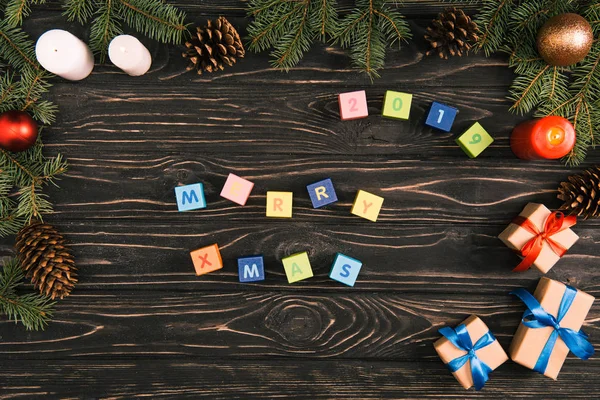 Vista superior de las letras felices de Navidad en cubos y cajas de regalo con ramitas de abeto en la superficie de madera - foto de stock