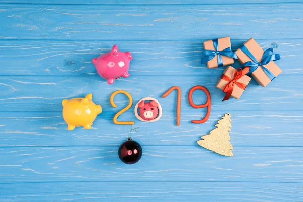 Vue du dessus du symbole 2019 avec tirelires roses et jaunes et cadeaux de Noël sur une surface en bois bleu — Photo de stock