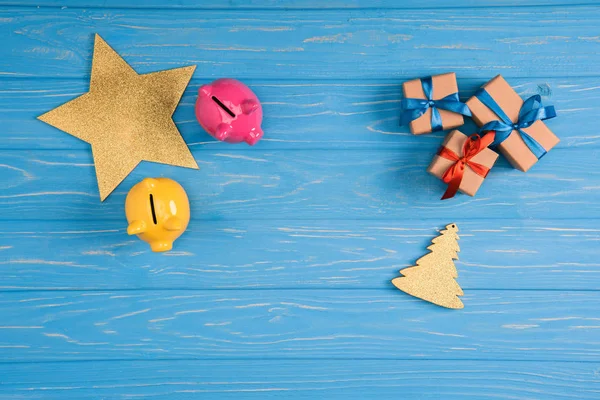 Vista superior de las orillas de cerdito amarillo y rosa, estrella, símbolo del árbol de Navidad y cajas de regalo superficie de madera azul - foto de stock