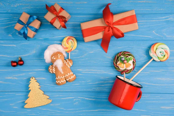 Top view of gingerbread cookie, lollipops and christmas presents on blue wooden surface — Stock Photo