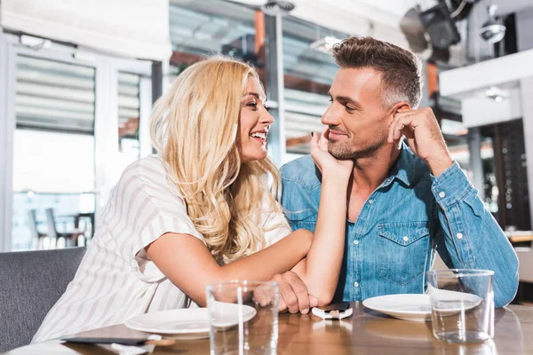 Sorridente fidanzata toccare fidanzato faccia a tavola in caffè — Foto stock