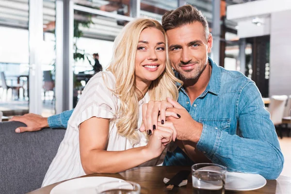 Feliz pareja abrazando y mirando a la cámara en la mesa en la cafetería - foto de stock