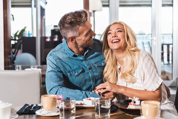 Bonito namorado olhando para rindo namorada na mesa no café — Fotografia de Stock