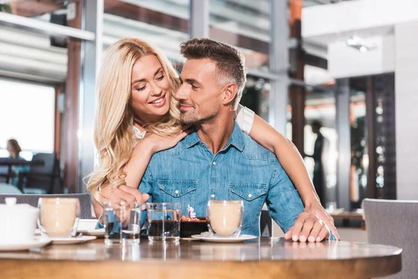 Sonrisa hermosa novia abrazando guapo novio durante la cita en la cafetería - foto de stock