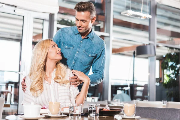 Bonito namorado de pé perto da mesa, abraçando namorada e eles olhando uns para os outros no restaurante — Fotografia de Stock