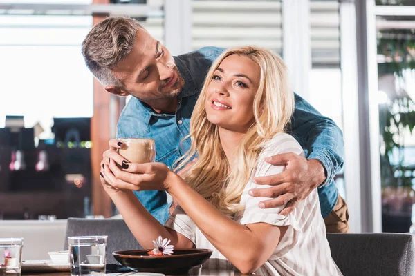 Handsome boyfriend hugging smiling girlfriend during date in cafe — Stock Photo