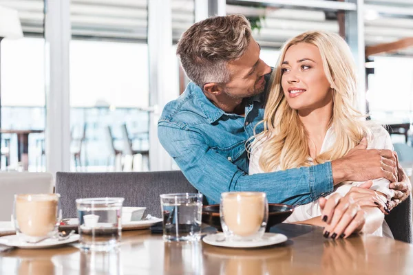 Guapo novio abrazando atractiva novia en mesa en café — Stock Photo