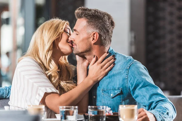 Cariñosa pareja heterosexual besándose en la mesa en la cafetería - foto de stock