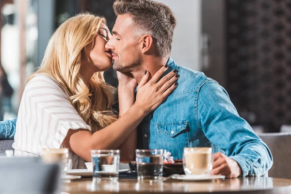 Cariñoso novio y novia besándose en la mesa en la cafetería - foto de stock