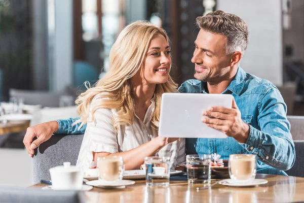 Ласковая пара с помощью планшета за столом в кафе и глядя друг на друга — стоковое фото