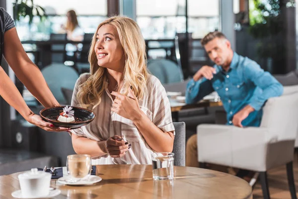 Cropped image of waiter showing dessert with flower to surprised woman in cafe — Stock Photo