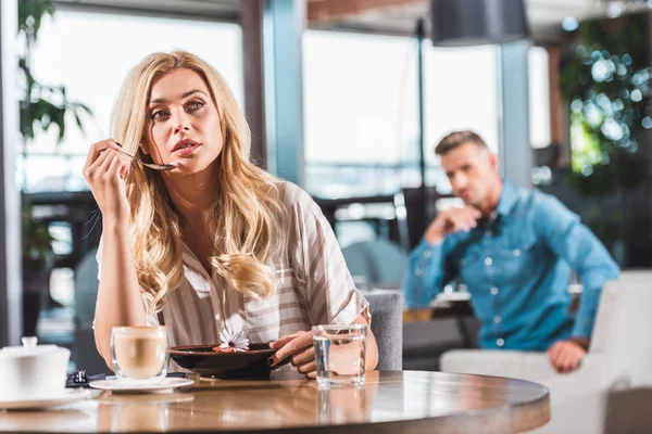 Pensive beautiful blonde woman eating dessert with flower in cafe — Stock Photo