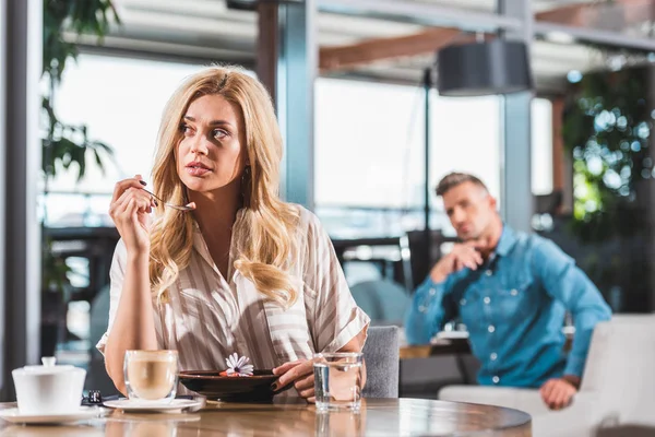 Bella donna bionda mangiare dessert con fiore in caffè e guardando altrove — Foto stock