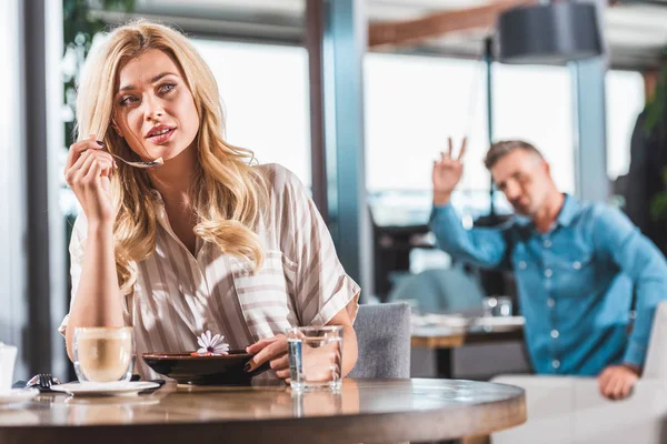 Schöne blonde Frau isst Dessert mit Blume im Café, Mann gestikuliert dem Kellner im Hintergrund — Stockfoto