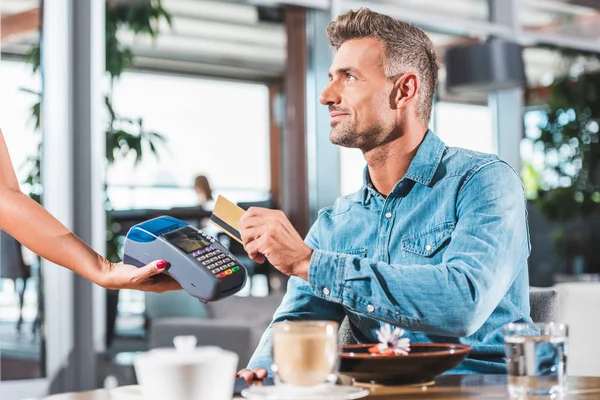 Vue latérale du bel homme payant par carte de crédit dans un café — Photo de stock