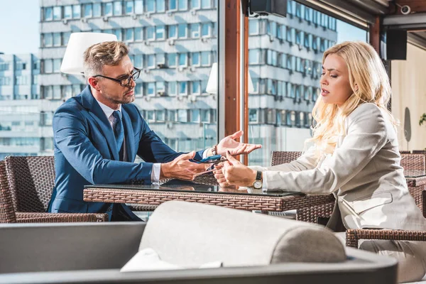Empresária e empresário falando no café e segurando smartphone com óculos — Fotografia de Stock
