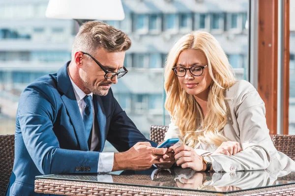 Retrato de socios comerciales utilizando smartphone durante la reunión en la cafetería - foto de stock