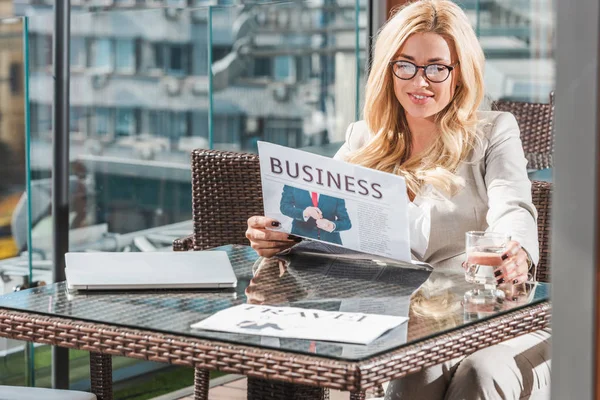 Hermosa mujer de negocios sonriente leyendo el periódico en la cafetería - foto de stock