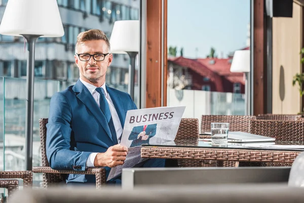 Portrait of stylish businessman in suit and eyeglasses with newspaper in cafe — Stock Photo