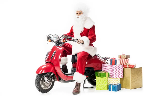 Уверенный Санта-Клаус в костюме сидя на скутере рядом подарочные коробки изолированы на белом фоне — стоковое фото