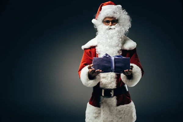 Alegre santa claus en traje mostrando caja de regalo aislado sobre fondo gris - foto de stock