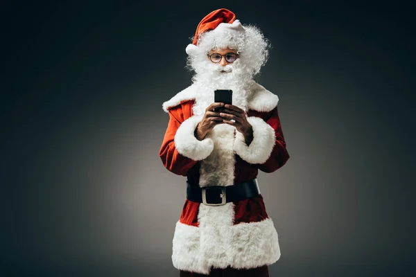 Glücklich Weihnachtsmann im Kostüm mit Smartphone isoliert auf grauem Hintergrund — Stockfoto