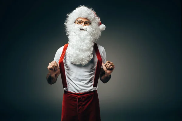 Щасливий Санта Клаус в окулярах тримає підтяжки, що стоять ізольовано на сірому фоні — стокове фото