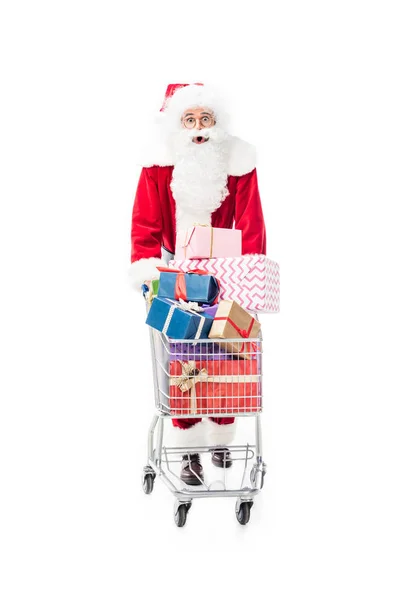 Shocked santa claus carrying trolley with pile of gift boxes isolated on white background — Stock Photo