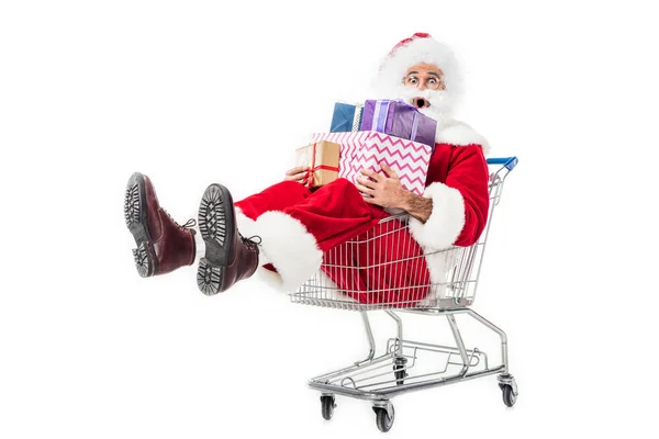 Шокований Санта Клаус тримає купу подарункових коробок у візку ізольовано на білому тлі — стокове фото
