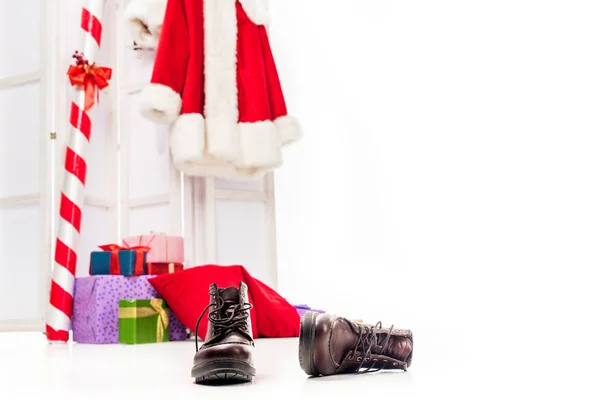 Vista da vicino di stivali e mucchio di scatole regalo e costume di Babbo Natale su schermo pieghevole dietro isolato su sfondo bianco — Foto stock