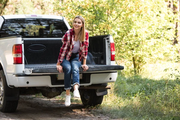 Attraktive junge Frau schaut weg und sitzt im Kofferraum eines Pick-ups im Freien — Stockfoto