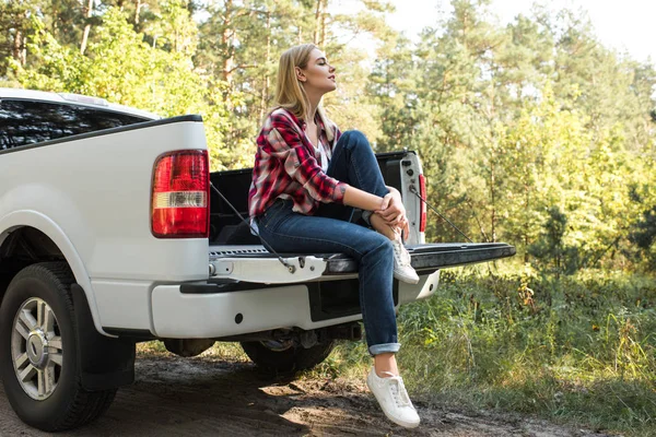 Vista laterale di giovane donna seduta nel bagagliaio di pick up auto all'aperto — Foto stock