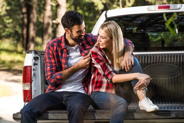 Sonriente joven pareja abrazando y sentado en coche tronco al aire libre - foto de stock