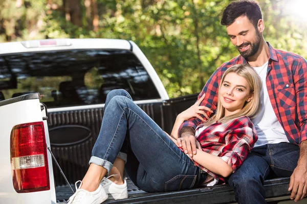 Feliz jovem mulher que coloca no namorado joelhos no carro tronco ao ar livre — Fotografia de Stock