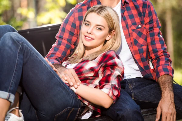 Smiling attractive woman laying on boyfriend knees on car trunk outdoors — Stock Photo