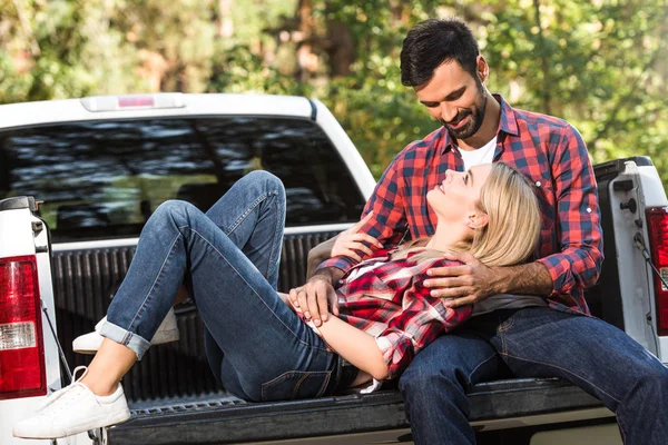 Foco seletivo da mulher que coloca no namorado joelhos no carro tronco ao ar livre — Fotografia de Stock