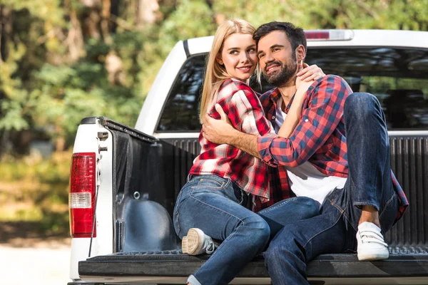 Heureux jeune couple embrassant l'autre sur le coffre de la voiture à l'extérieur — Photo de stock