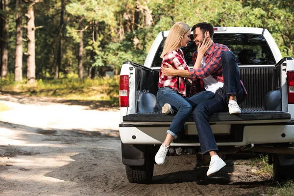 Vue latérale du jeune couple s'embrassant et se regardant sur le coffre de la voiture à l'extérieur — Photo de stock