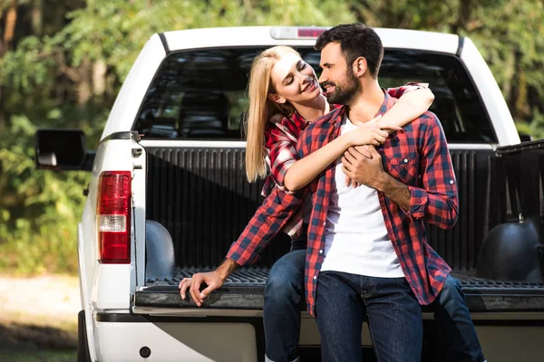 Young cheerful couple embracing each other on car trunk outdoors — Stock Photo