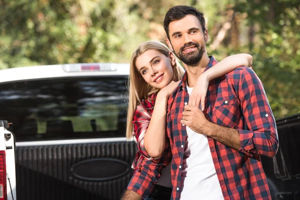 Foco seletivo de jovem casal abraçando uns aos outros no carro tronco ao ar livre — Fotografia de Stock