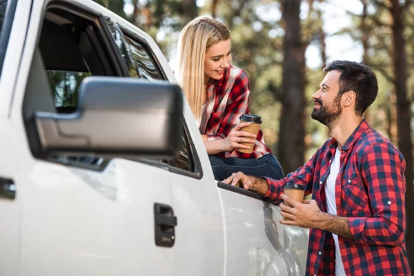 Cheerful young couple with paper cups of coffee near pick up car outdoors — Stock Photo