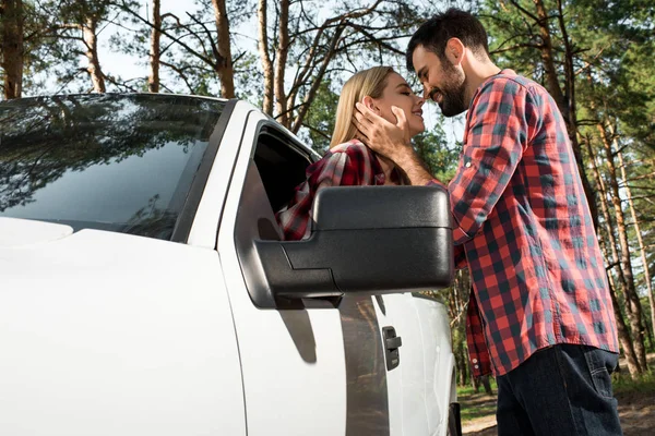 Low angle view of man kissing girlfriend sitting in pick up car outdoors — Stock Photo