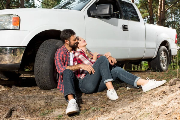 Feliz jovem casal sentado no chão e abraçando perto pegar carro ao ar livre — Fotografia de Stock
