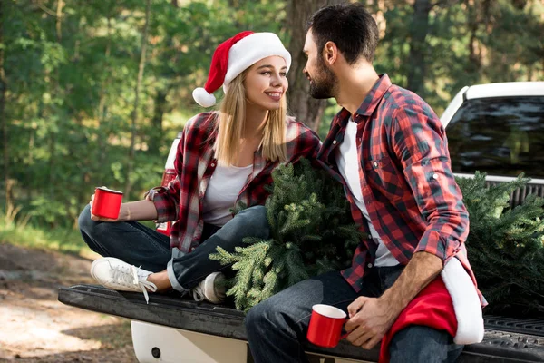 Attrayant femme avec petit ami tout en étant assis sur le coffre de la voiture avec arbre de Noël en plein air — Photo de stock